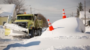 Abandon car marked by orange cones is buried under snow as a snowplow passes by in Buffalo